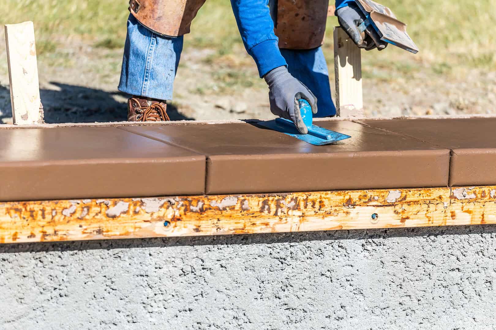 Construction Worker Using Trowel On Wet Cement Forming Coping Around New Pool.